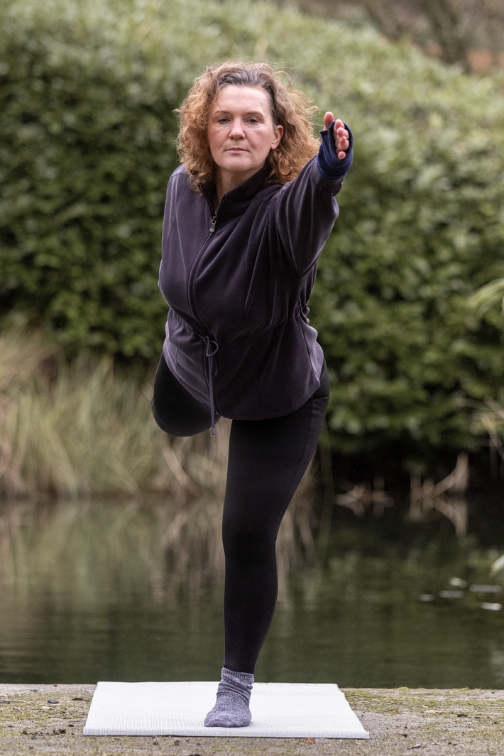Woman practicing yoga outdoors by a body of water wearing Fyness