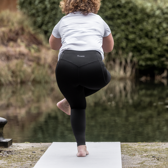 Person practicing yoga outdoors by a body of water wearing Fyness Motionline leggings.