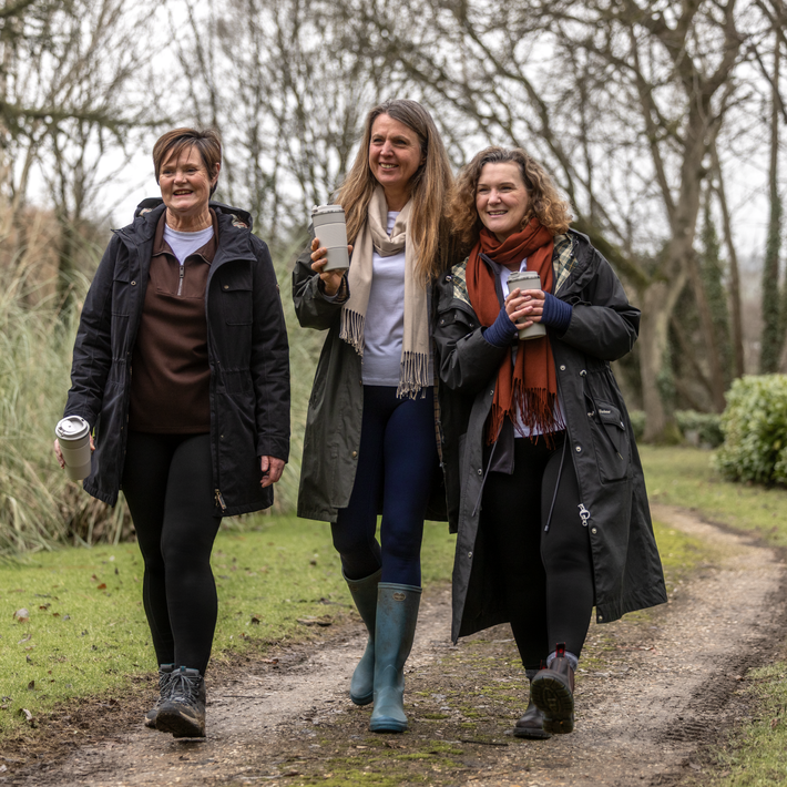 Three women walking outdoors on a path, holding coffee cups.